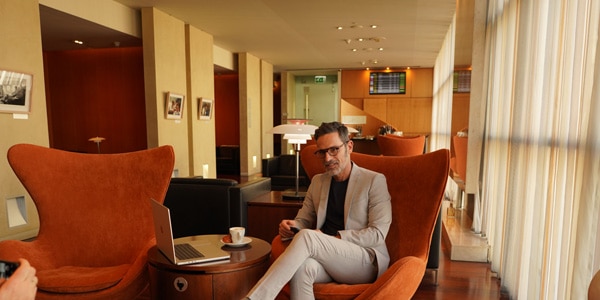 A man sits on a chair with a cup of coffee and a laptop next to him